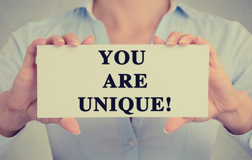 Closeup businesswoman hands holding white card sign with you are unique text message isolated on grey wall office background. Retro instagram style image